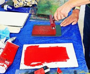 image of a hand holding a roller and rolling out red ink onto a piece of lino