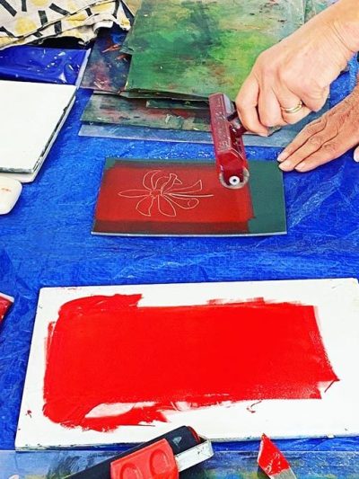 image of a hand holding a roller and rolling out red ink onto a piece of lino