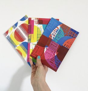 hand holding three A5 notebooks with abstract covers.