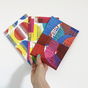 hand holding three A5 notebooks with abstract covers.