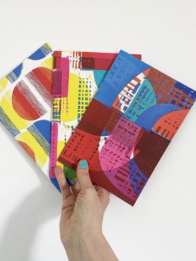 hand holding three A5 notebooks with abstract covers.