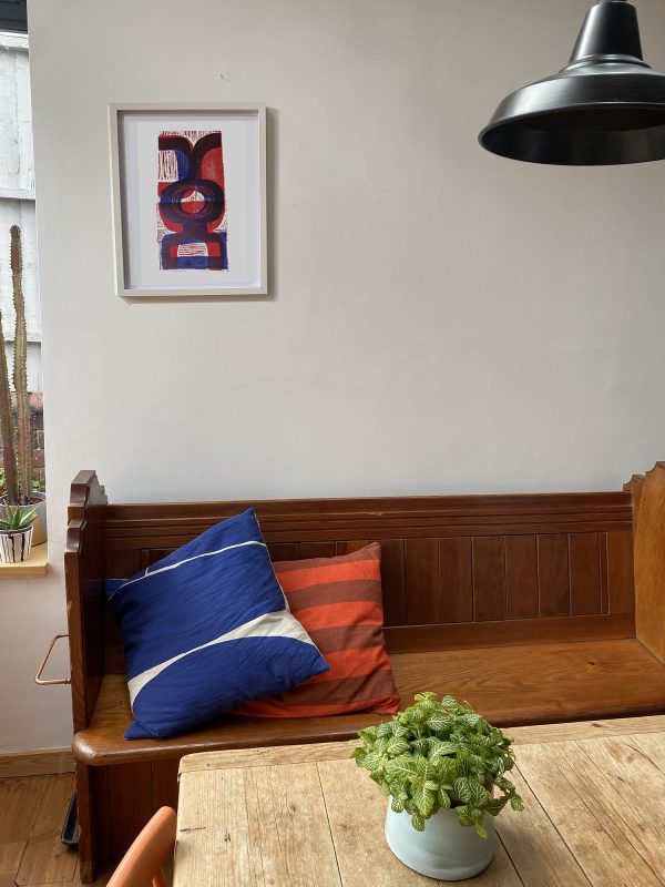 Room with wooden bench with cushions on and above hangs 'Blue & Red' in a white A2 frame