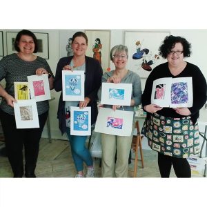 Four smiling ladies holding their linocut prints after a successful day of printing on my workshop.