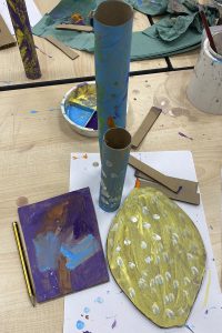 Table showing painted cardboard tubes and flat shapes and a palette with paint in.